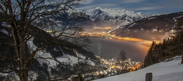 Nächtlicher Blick vom schneebedecktem Berg in ein Tal mit mehreren beleuchteten Ortschaften